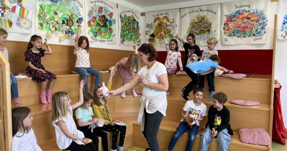 Kinder sitzen in der Bibliothek und hören der Lehrerin zu