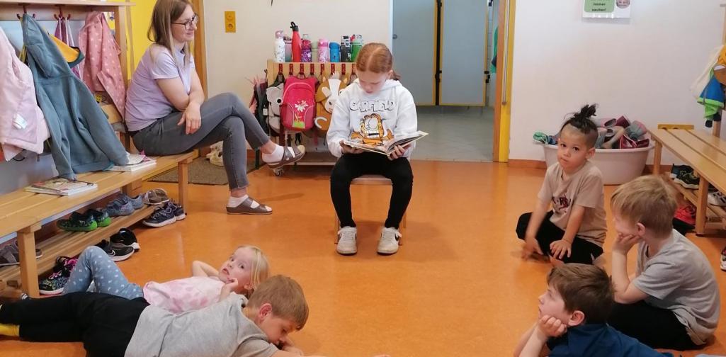 Eine Schülerin liest im Kindergarten ein Buch vor.